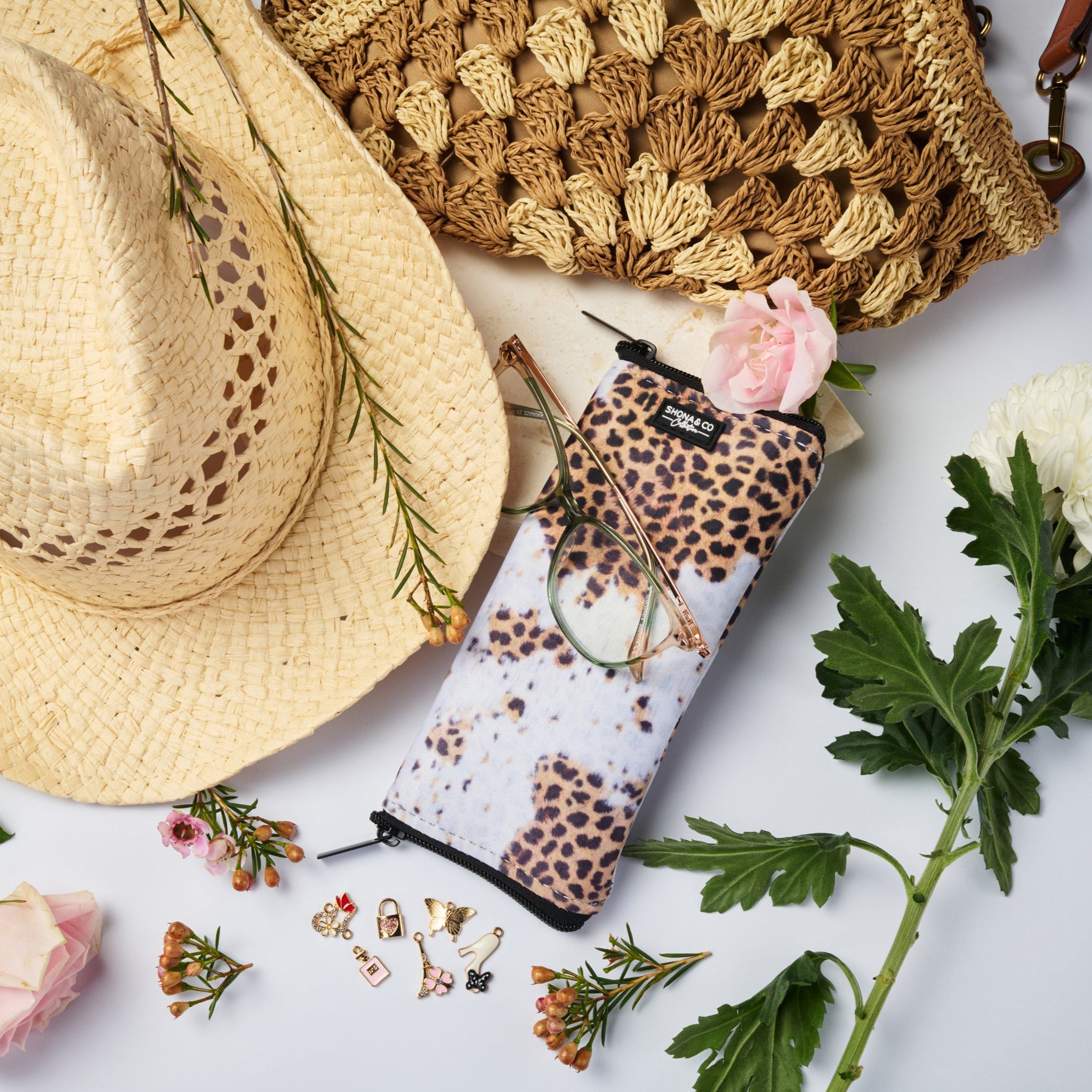 Leopard print handbag, straw hat, and floral arrangement on a light surface