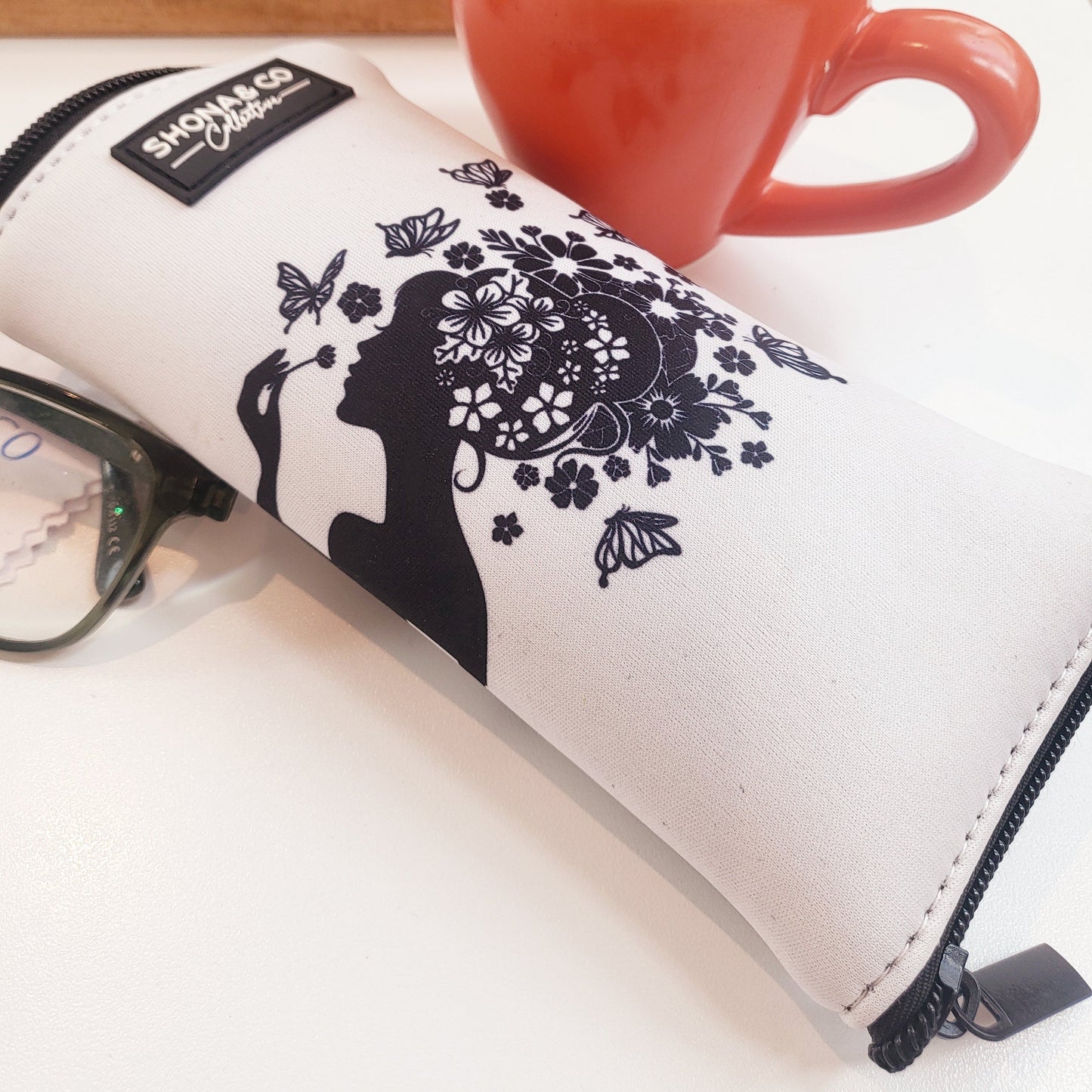 White pouch with black floral design on a surface next to a red mug with tea.